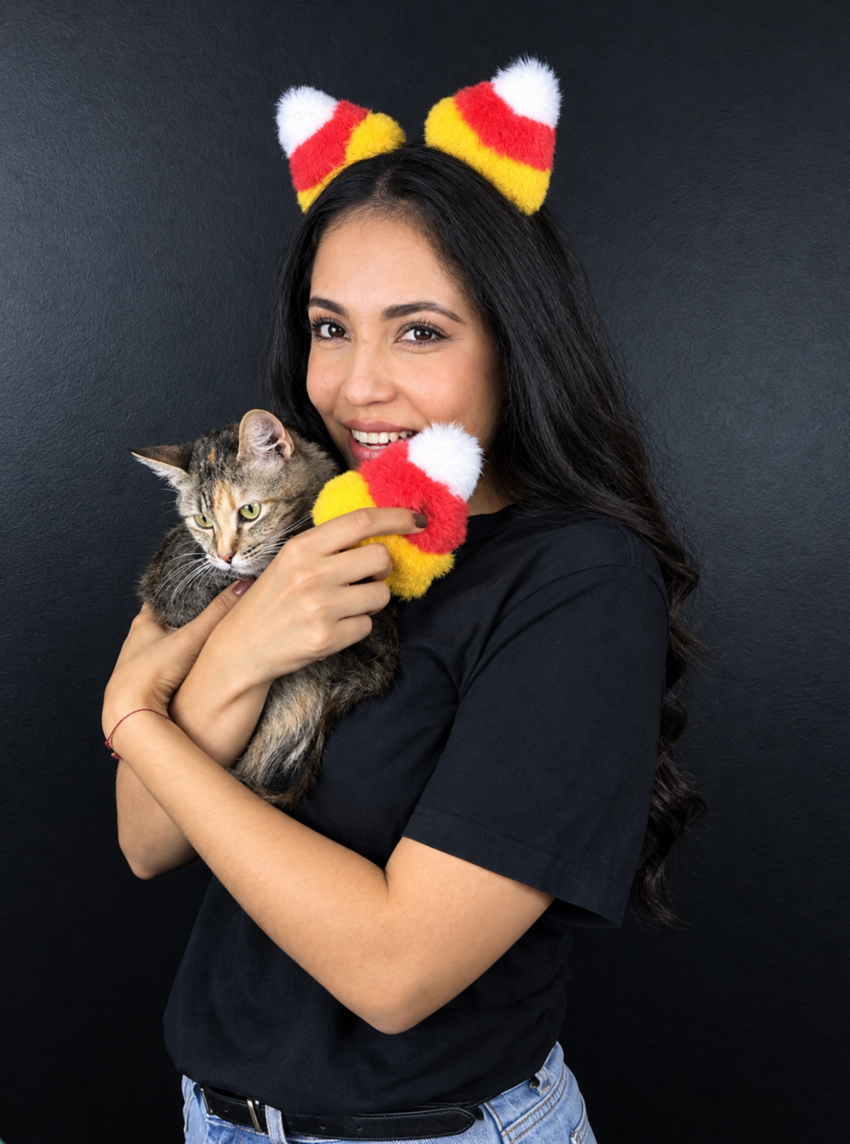 Woman wearing candy corn cat ears headband while holding a tabby cat